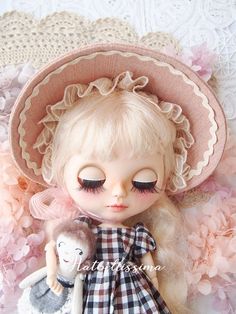 the doll is wearing a hat and holding a stuffed animal in her arms, with pink flowers surrounding it