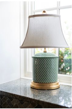 a lamp sitting on top of a table next to a window with a white shade