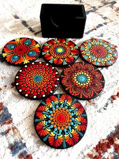 six coasters with colorful designs on them sitting on a rug next to a black box