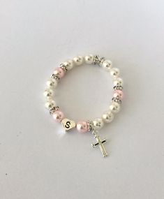 "Gift someone special this timeless gift of a classic pearl bracelet. Swarovski 6mm pearls in white and rosaline circle the wrist and frame a sterling silver heart initial bead. Sparkly rhinestone rondelles add a touch of glitz, and a sterling silver cross hangs by the initial. The bracelet is created on elastic cord for easy on/off. - - - -> WHAT SIZE SHOULD YOU BUY? The listing photo shows a 6 1/2\" bracelet. It's always best to measure a bracelet that currently fits the recipient, but if y Pearl Charm Jewelry For First Communion, Elegant Adjustable Rosary Bracelet For Birthday, Elegant Pearl Rosary Bracelet For Baptism, Classic Personalized White Pearl Bracelet, Elegant Pearl Jewelry For Confirmation, Classic Adjustable Pink Bracelets, Adjustable Classic Pink Bracelets, Classic Personalized Pearl Bracelet, Personalized Classic Pearl Bracelet