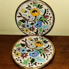 two decorative plates sitting on top of a wooden table next to a wall and floor