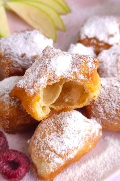 powdered sugar covered pastries with raspberries and an apple in the background