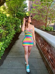 a woman is walking down the sidewalk wearing a colorful dress and blue tennis shoes with her hand on her head