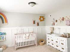 a baby's room with a crib, dresser and rainbow wall hangings