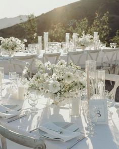 a table set up with white flowers and candles for an outdoor wedding reception in the mountains