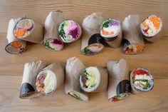 there are many different types of sushi rolls on the table, all wrapped in brown paper