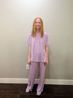 a woman standing in front of a wall wearing purple pants and a t - shirt