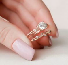 a woman's hand holding a gold ring with two leaves on it and a diamond in the middle