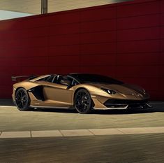 a gold colored sports car parked in front of a red wall