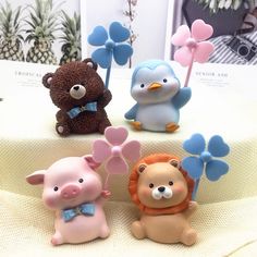 there are four small toy animals sitting on the table with each one holding a pinwheel