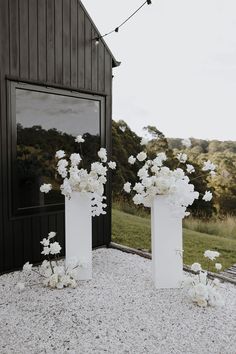 two tall white vases filled with flowers on top of gravel