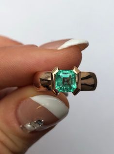 a close up of a person holding a ring with an emerald stone in it's center