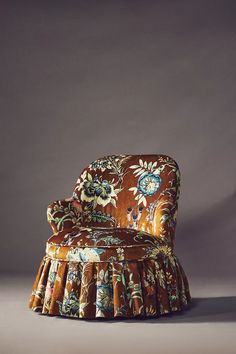 an upholstered chair with a flowered design on the back and pleated skirt