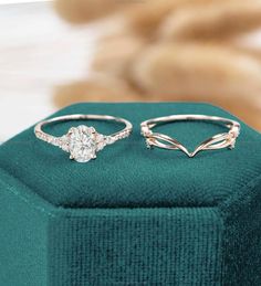 two engagement rings sitting on top of a green velvet ring box next to each other