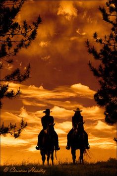 two people riding horses in front of an orange sky