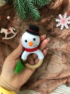 a hand holding a crocheted snowman ornament next to christmas decorations