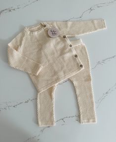 Get ready for cuteness overload with our baby sweater and pants set! Featuring a textured pattern, this long sleeve sweater has buttons on the side for easy dressing. The matching pants have an elastic waistband for a comfortable fit. Perfect for your little one's playful adventures! Cozy Playtime Sets For Fall, White Knitted Long Sleeve Set, Soft Knit Long Sleeve Sweater For Playtime, Cream Long Sleeve Sets For Fall, White Long Sleeve Sets With Button Closure, Fall Long Sleeve Sets With Button Closure, Beige Long Sleeve Sets With Buttons, Baby Sweater, Our Baby