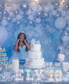 a woman standing in front of a cake surrounded by white and blue desserts with snowflakes