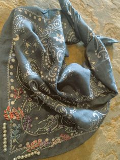 a blue scarf with flowers and beads on it sitting on top of a stone wall