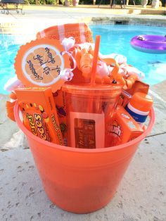 an orange bucket filled with lots of candy next to a swimming pool