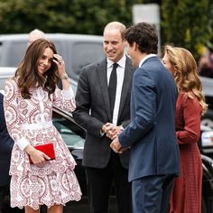 two men and a woman shaking hands while standing next to each other in front of cars