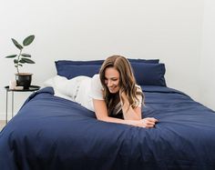 a woman laying on top of a blue bed next to a green potted plant