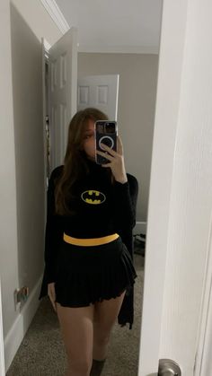 a woman taking a selfie in the mirror wearing a batman shirt and short skirt