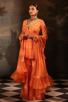 Tangerine peplum kurta with floral print and mirror, thread, pearl, bead, gota embroidered neckline. Paired with gharara and dupatta.
Components: 3
Pattern: Printed, Embroidery
Type Of Work: Floral, mirror, thread, pearl, bead, gota
Neckline: Plunge V neck
Sleeve Type: Full sleeves
Fabric: Georgette, Organza, Lining: Crepe
Color: Orange
Other Details: 
Length:
Kurta: 34 inches
Gharara: 42 inches
Sheer dupatta
Pleated frill hem
Occasion: Sangeet - Aza Fashions Sheer Dupatta Georgette Peplum Set, Georgette Peplum Set With Sheer Dupatta, Anarkali Dress With Sheer Dupatta And Peplum Shape, Festive Peplum Dress With Sheer Dupatta, Festive Georgette Sharara With Peplum, Designer Georgette Sharara For Diwali, Georgette Sharara For Diwali Designer Wear, Bollywood Style Peplum Dresses For Diwali, Georgette Peplum Sharara For Eid