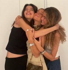 three women hugging each other in front of a white wall