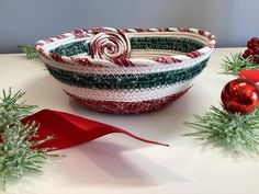 a red, white and green striped bowl next to christmas ornaments on a table with ribbon