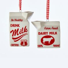 two ceramic milk jugs hanging from red and white ribboned strings, each with a cow's head on it