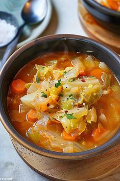 there is a bowl of soup with carrots, cabbage and other vegetables in it