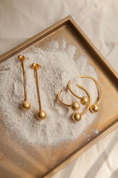 three pairs of gold earrings sitting on top of a tray filled with white powder and other items