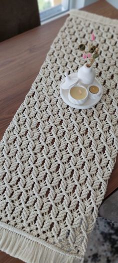 a crocheted table runner with a tea pot and saucer sitting on it