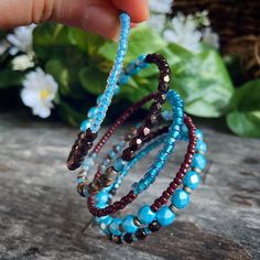 a hand is holding three bracelets with beads on them and flowers in the background