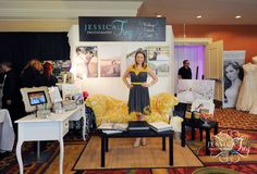 a woman standing next to a couch in a room with pictures on the wall and tables