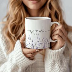 a woman is holding a coffee mug with lavender flowers on it and she has her hands in front of her face