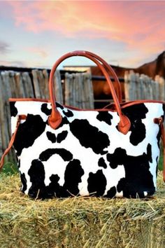 This fun fuzzy fabric bag will send you over the moon! Black and white cow print puts a western twist on this trendy tote. Cognac vinyl detailing, metal feet, and magnetic button top closure. Cognac nylon inner lining and zipper pocket. 22'' W x 14' H x 3'' D Rectangular Cow Print Travel Bag, Trendy Cow Print Bags For Everyday Use, Black Bag With Cow Print For Everyday Use, Casual Everyday Bag With Cow Print, Casual Cow Print Bags For Daily Use, Cow Print Purse, Moon Black And White, Black And White Cow Print, Printed Leather Bag