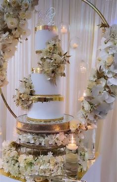 a three tiered wedding cake with white flowers and gold trimmings on a table