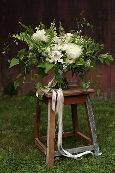 a bouquet of flowers sitting on top of a wooden stool in the middle of grass