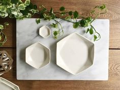 two white plates on a marble table with greenery next to them and a plant in the background