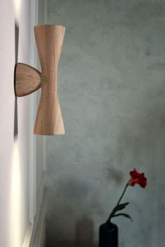 a vase with a flower in it next to a wall mounted wooden object on the wall