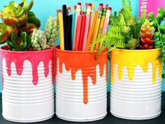 three tin cans filled with different colored pencils and plants