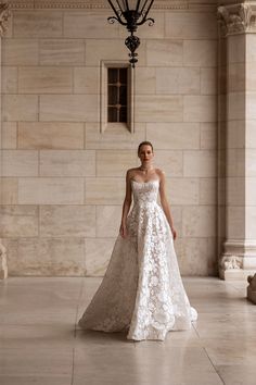 a woman in a white wedding dress standing on a stone floor next to a chandelier