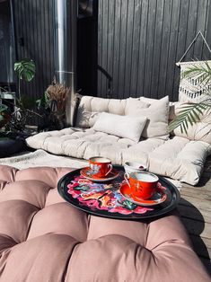 two cups of coffee sit on a tray in front of a couch with pillows and potted plants