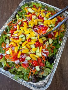 a salad in a foil container with tongs on the side, ready to be eaten