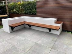 a white bench sitting on top of a cement slab next to a wooden fence and shrubbery