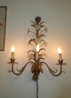 a wall mounted light fixture with three candles on each arm and an ornate flower design