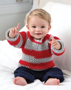 a toddler sitting on a bed holding a toothbrush and pointing at the camera