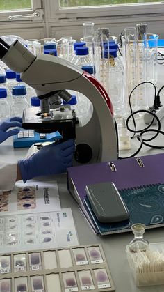 two people in lab coats and gloves looking through microscopes at items on a table